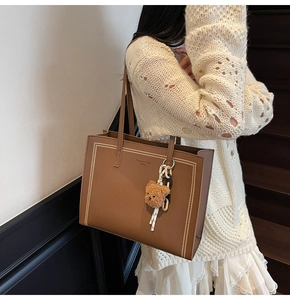 Detail view of brown tote bag with white stitching and plush bear charm on model
