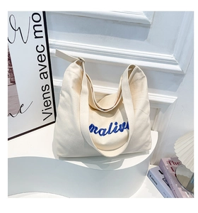 Detail of off-white canvas tote bag with bold blue embroidered lettering on geometric stand