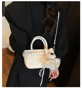 Détail d'un sac à main en cuir verni blanc avec charm chien en peluche sur un blazer sombre