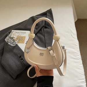 Detail of milk tea color crescent bag with glossy finish and silver G-shaped pendant