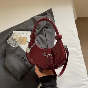 Detail of burgundy crescent handbag with glossy patent leather and knot handle detail
