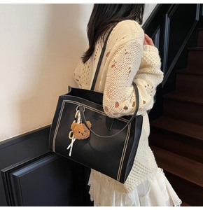 Detail view of black lychee leather tote bag with metal rivets and a cute bear charm