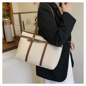 Chic cream bucket tote bag with brown trim shown on shoulder in a cafe setting