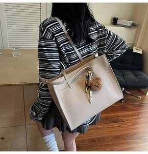 Detail view of cream tote bag with wavy trim and plush bear charm on model's shoulder