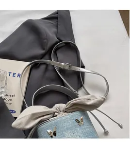 Détail du sac seau en denim bleu clair avec grand nœud crème et boucle papillon argent