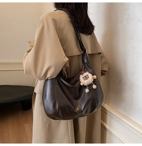 Dettaglio borsa tote in pelle marrone scuro con logo del marchio e ciondolo a forma di agnello