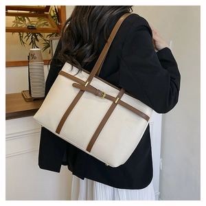 Detail of minimalist cream leather tote bag with brown straps and gold metal buckle accents