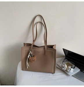 Brown litchi leather tote bag shown with bear charm and laptop in office setting