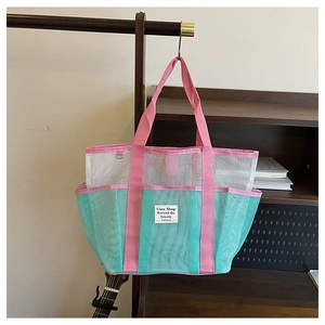 Close-up of mesh beach bag showing blue and white paneling with pink handles and woven label