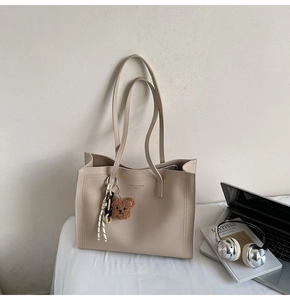 Detail of beige lychee leather tote bag with Fashion Trend text and plush bear charm
