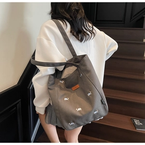 Model wearing grey canvas tote bag with puppy embroidery on indoor wooden stairs