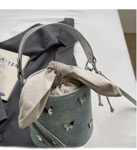 Détail du sac seau en denim bleu clair avec papillon argenté et nœud de serrage élégant