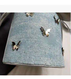 Détail du sac seau en denim avec papillons métalliques et rivets argentés brillants