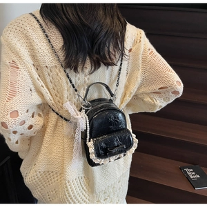 Détail du mini sac à dos en cuir verni noir avec dentelle blanche et nœud élégant