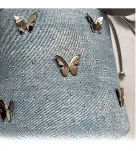 Détail d'un sac en denim bleu clair avec breloque papillon argentée et rivets en métal