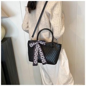 Detail of black tote bag featuring vertical pleated texture and checkered scarf bow ornament