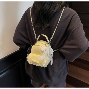 Détail du mini sac à dos jaune avec bordure en dentelle et pendentif nœud en perles