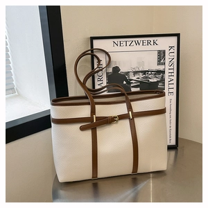 Detail of white lychee leather tote bag with brown straps on a metallic table