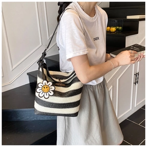 Detail of striped woven tote bag with a white daisy smiley charm on a model