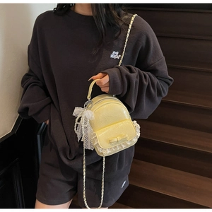 Détail du mini sac à dos jaune en cuir verni brillant avec bordure en dentelle blanche