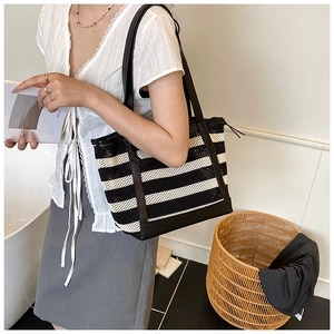 Detail of a large black and white striped woven tote bag with durable leather straps