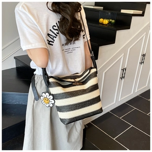 Detail of striped straw tote bag featuring leather strap and sunflower charm pendant