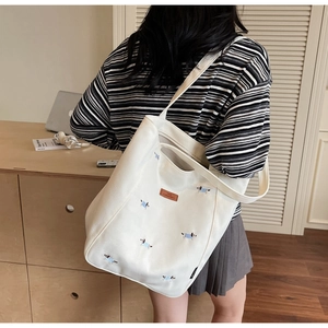 Detail of white canvas tote bag featuring dog embroidery and premium brown leather label