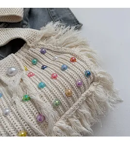 Detailed close-up of cream knit bag with colorful pearly beads and fringe edge details