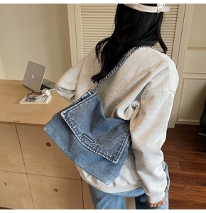 Detail of blue denim tote bag with chain strap shown in a casual lifestyle setting
