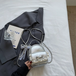 Détail du sac à dos argenté avec dentelle, pendentif perle et texture métallique chic