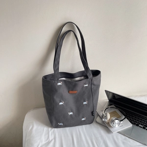 Detail of dark grey canvas tote with embroidered dogs, laptop, and books on white background