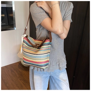 Close-up of a striped straw woven tote bag with brown leather straps and white tassels