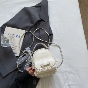 Détail d'un mini sac à dos crème avec dentelle, nœud et bandoulière en perles
