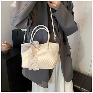 Chic beige pleated tote bag with checkered bow detail worn on the shoulder by a model