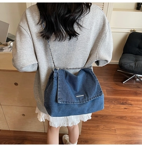 Detail of blue denim tote bag with metal chain strap worn by model in cozy interior