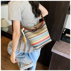 Detail of colorful striped straw tote with brown leather strap and decorative fringe
