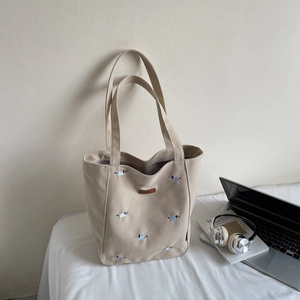 Detailed view of cream canvas tote bag with embroidered dog patterns and a leather patch
