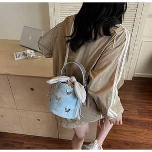 Détail du sac seau en denim bleu clair avec breloques papillon et cordon porté par un modèle