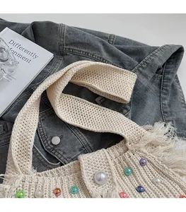 Detail of hand-woven beige tote with colorful beads and fringe over denim jacket