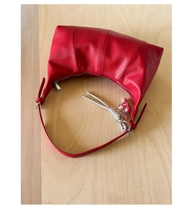 Dettaglio borsa hobo in pelle rossa a grana con hardware argento e ciondolo a nodo