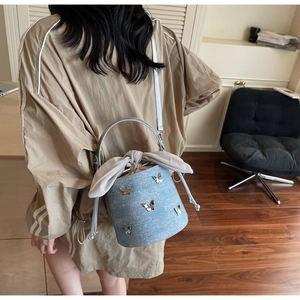 Détail du sac seau en denim avec des papillons argentés et un grand nœud décoratif gris