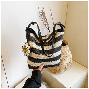 Detail of woven straw tote bag with black stripes, wood horn buckle and sunflower charm