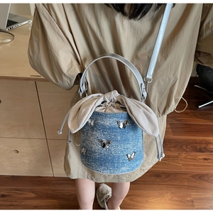 Détail du sac seau en denim avec appliques papillons en métal et cordon de serrage