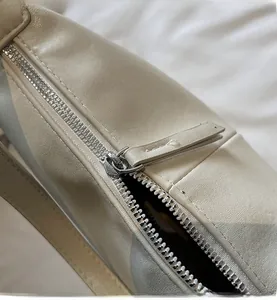 Gros plan détaillé de la fermeture éclair argentée et tirette en cuir sur sac beige