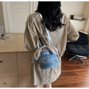 Détail du sac seau en denim bleu avec breloques papillon et cordon à oreilles de lapin