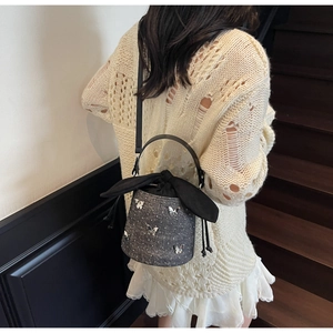 Détail du sac seau gris foncé avec breloques papillon argentées et décoration de nœud lapin