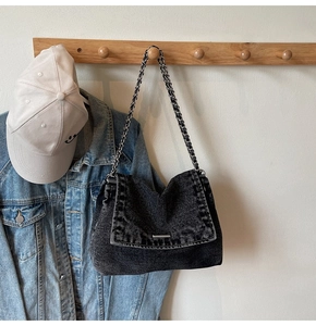 Detail of black denim shoulder bag with frayed edges and silver chain strap on a wooden hanger