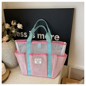 Detail of a mesh beach bag with pink trim, blue handles, and multiple side pockets