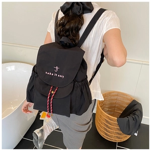 Dettaglio zaino in tela nera con ricamo rosa e decorazione con coulisse rossa e bianca