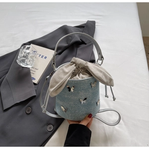 Détail du sac seau en denim avec breloques papillons argentées et cordon beige